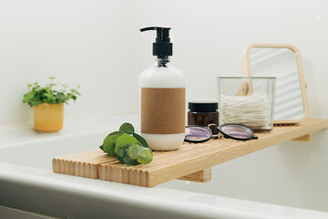 Bathtub wooden tray with beauty cosmetic bottles and accessories in a modern interior scandinavian bathroom with white tiles as a background. Home decor with candles and green plants.