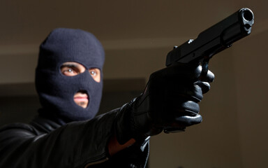Murderer with balaclava holds gun in leather jacket and gloved hand background.