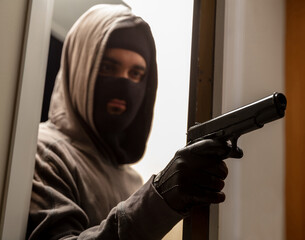 Criminal with balaclava holds gun in leather gloved hand behind door. Terrorism, violence