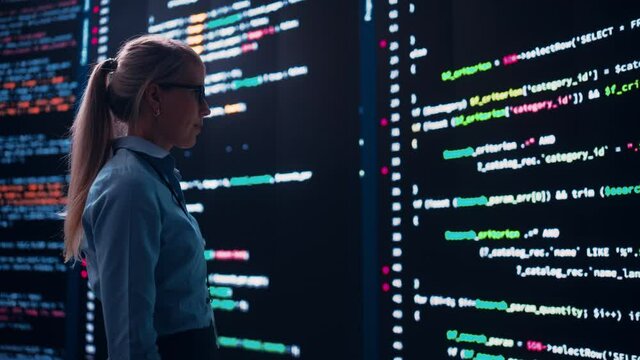 High-Tech Startup Concept: Innovative Female Software Engineer Standing and Doing Big Data Analysis on Wall Screen Showing Porgramming Code. Developing Futuristic e-Commerce App with Machine Learning