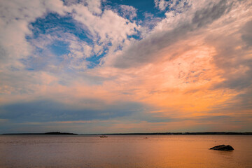 Dramatic cloudscape with rising sun over the sea. Zen-like rock in the glowing reflections of the ocean at dawn.