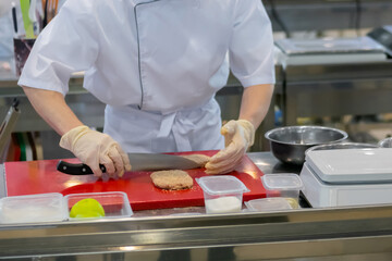 Chef hands holding knife and preparing breaded minced meat cutlet on red cutting board - close up. Professional cooking, cookery, gastronomy and food concept