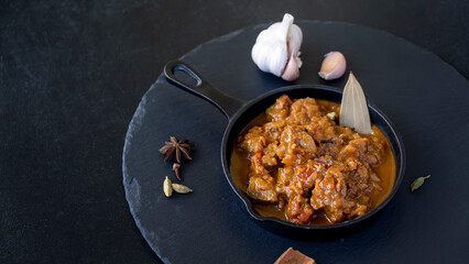 Traditional Indian beef curry served iron-cast. World cuisine. Black slate background.