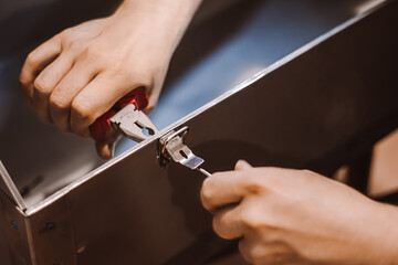Furniture assembler mechanic works with screwdriver. Male worker installs metal latch. Hands hold repair tool. Small business support.