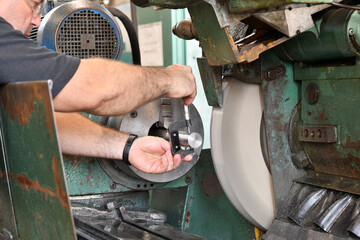 The worker measures the part with a micrometer on a cylindrical grinding machine.