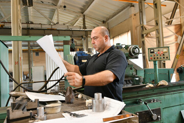 A worker reads a technical drawing near a metalworking machine before starting work.