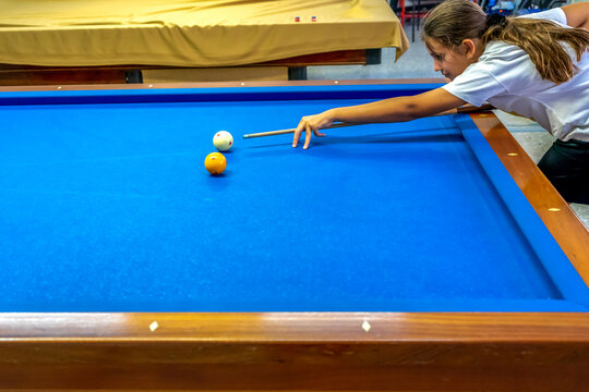 Teenage girl takes aim at a ball sitting on the pool table. Carom billiards or Frecnh billiard