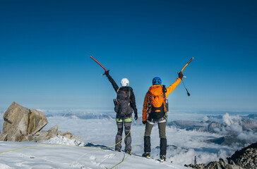 Couple dressed mountaineering clothes with backpacks rising arms with ice axes and enjoying views...