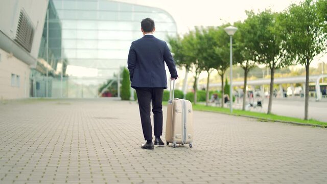 Rear view Asian tourist businessman walks public transport building with luggage the urban background city street Man in formal suit trip. Business traveler pulling suitcase in modern airport terminal