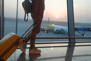 girl with a yellow suitcase standing at the airport and waiting for the plane.