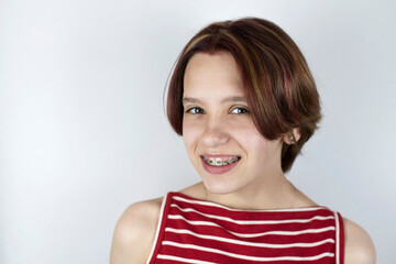 Fototapeta premium Teen girl mysteriously smiling on a light background, she knows the secret of a beautiful smile - straight healthy teeth thanks to braces. Dental concept