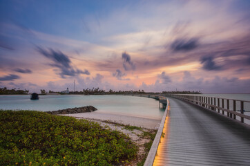 Wooden bridge over the beautiful Maldivian Indian or ocean with sunset sky. Crossroads Maldives, july 2021