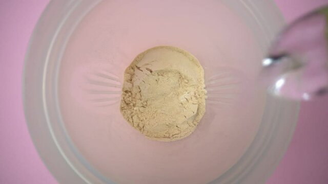 Extreme macro video, an athlete pours water into a shaker with protein, sports nutrition, for gaining muscle mass. Top view. Slow motion.