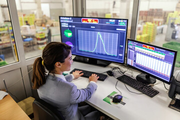 Working at a computer in back office. Woman in an elegant suit sits in front of a large computer screen and does analysis and calculations Online business and research, business performance monitoring