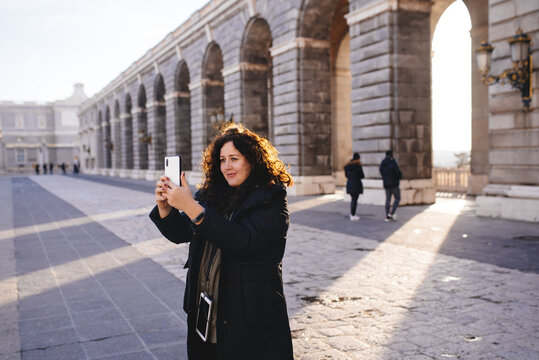 smiling girl taking a selfie on the phone in a European city, in a winter jacket, Royal Palace of Madrid