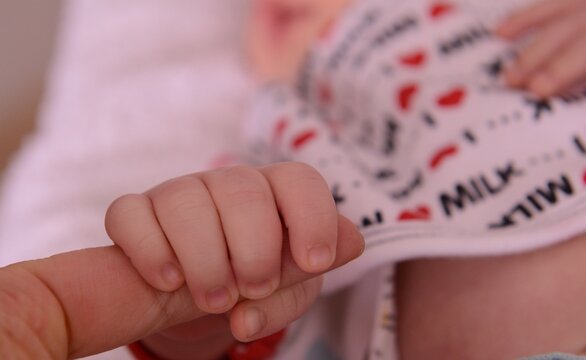 Baby in white and red  holding persons finger close-up
