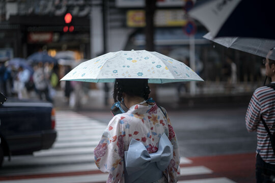 Back view of woman in kimono holding an umbrella walking on pedestrian lane