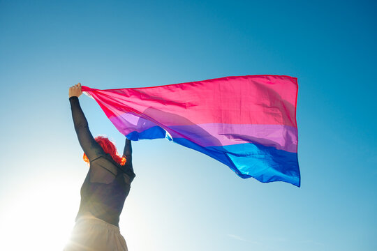 Back view of woman waving colorful flag under blue sky