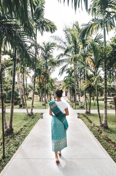 Back view of woman wearing traditional outfit waking a pathway between palm trees