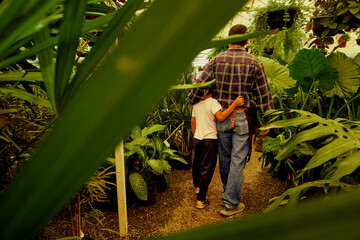 Father and son gardener hugging and walking surrounded by plants in a greenhouse