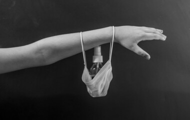 Grayscale photo of a Hand holding a facemask and sanitizer