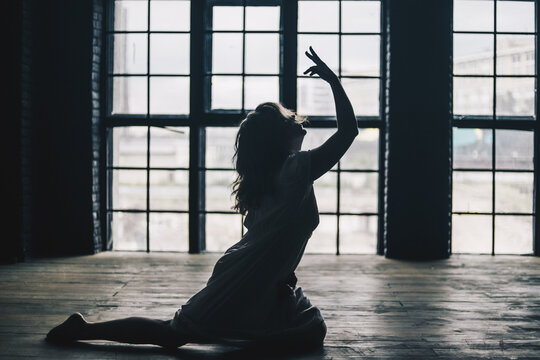 grayscale photo of a woman dancing beside window