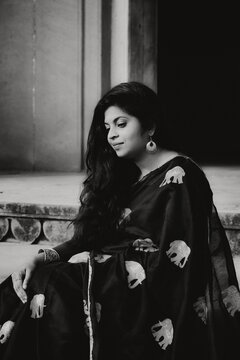 grayscale portrait of Woman in sari sitting on a concrete floor outdoors of hindu temple