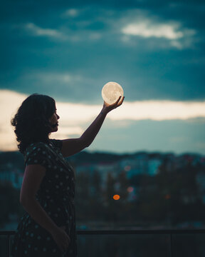 Illusion of woman holding the moon in sky