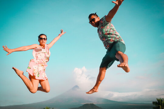 Man and woman jumping in the sky with mountain at the distance during daytime