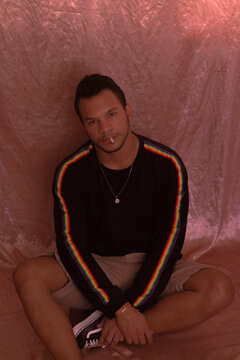 Man in black top sitting on ground against pink background