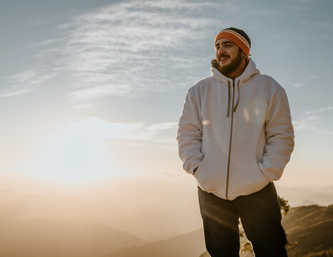 Man in offwhite jacket and colorful kint cap standing high in the mountain