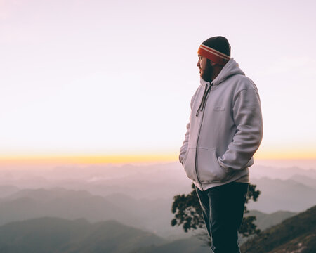 Man in light hoodie and colorful knit cap standing high in the mountain