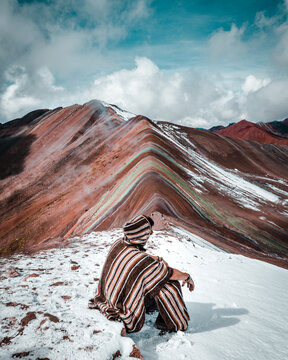 Man in Peruvian outfit looking at Vinicunca Rainbow Mountain in winter