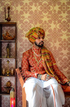 Man sitting on chair wearing Indian traditional outfit before pattern wallpaper