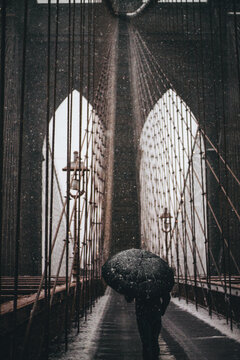 Person holding umbrella walking on a bridge under the rain