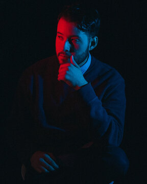 Portrait of man wearing sweater and collared shirt in red dim lit room
