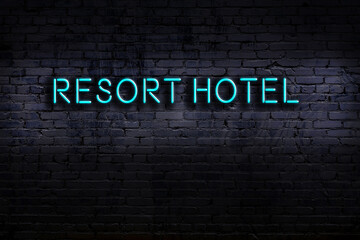 Neon sign. Word resort hotel against brick wall. Night view