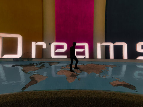 Silhouette of man walking on world map with word " Dreams " in the background