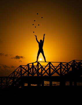 Silhouette of person throwing balls and standing on a staircase near body of water during sunset