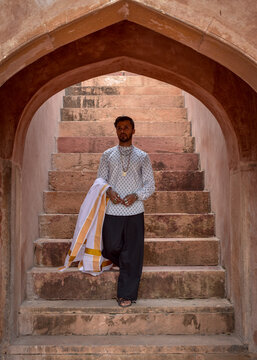 South Asian man wearing kurta and textile standing on concrete arched outdoor staircase