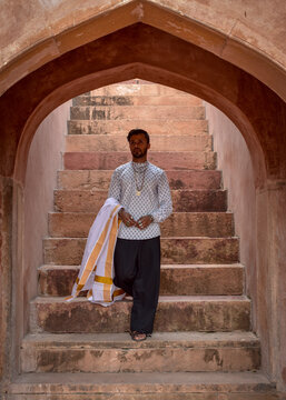 South Asian man wearing kurta and textile standing on concrete arched outdoor staircase