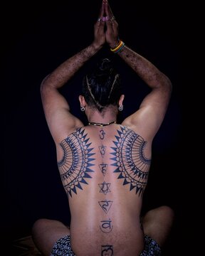 Topless man with mandala back tattoos meditating
