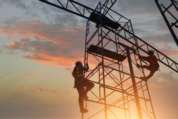 Two construction workers climbing a scaffolding during sunset