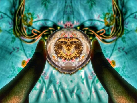 Two fingers holding clear glass ball showing golden patter