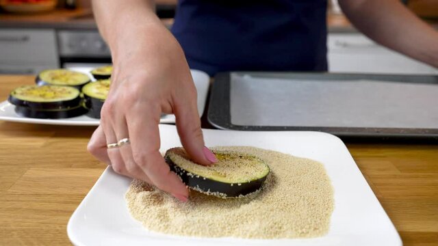the chef rolls the pieces of eggplant in breadcrumbs and places them in a baking dish in the oven. home food making process