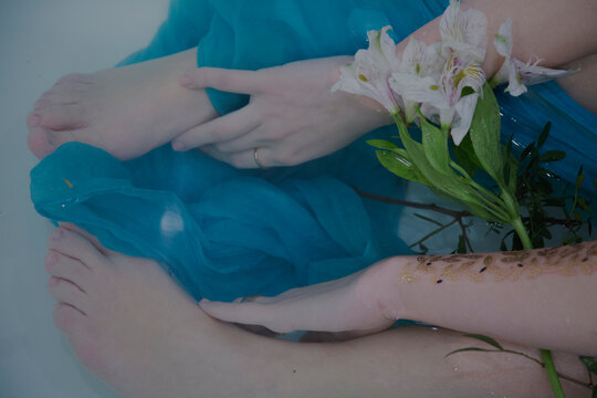 White Flowers between woman's feet and arms submerged in water with blue fabric in bathtub