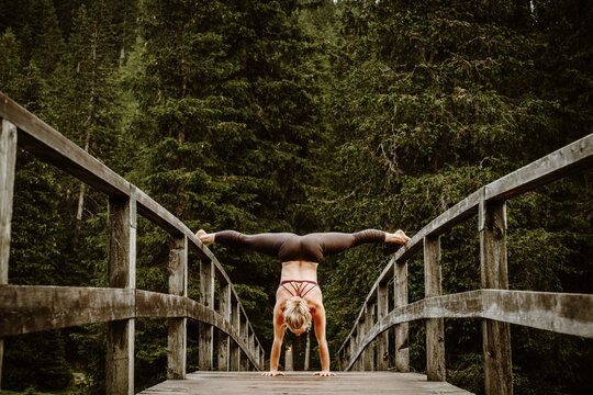 Woman doing a handstand and doing full split on wooden bridge