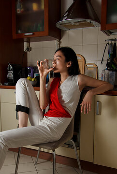 Woman drinking from clear glass sitting on a chair in the kitchen