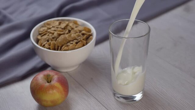 pouring milk into a glass glass on a wooden table. Healthy breakfast in the morning. Cereals, fruits and milk