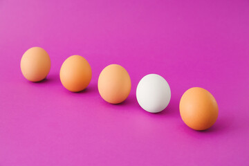 White egg among brown ones on color background. Concept of uniqueness